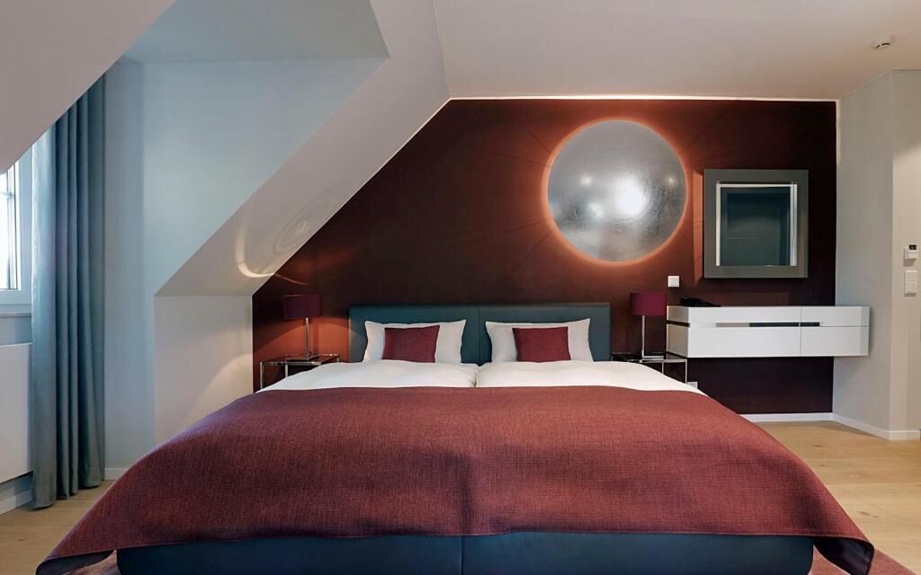 A modern bedroom with a large bed, a circular light feature on the wall, and a minimalist dresser.