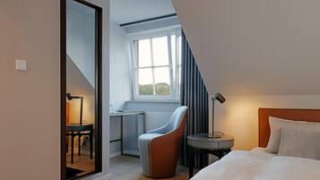 Habitación de hotel moderna con una cama grande, un escritorio, una silla y una ventana con cortinas.