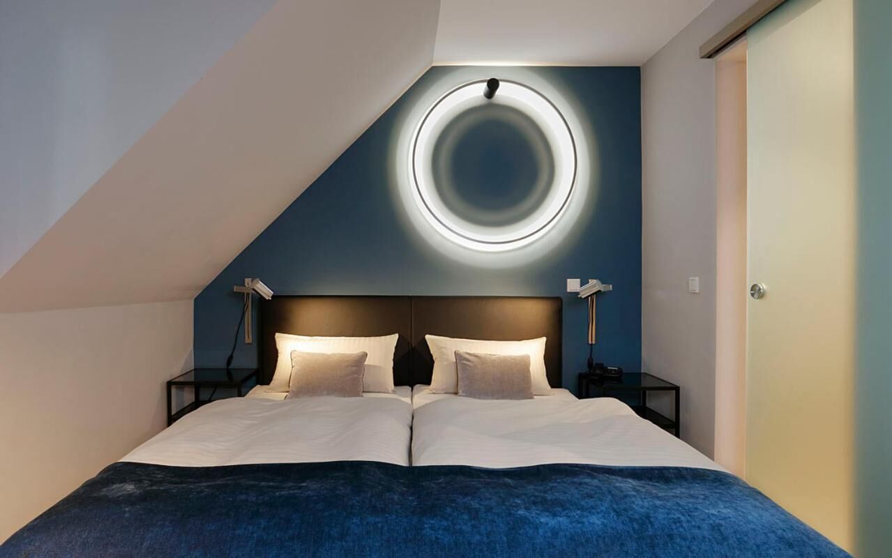 A modern bedroom with a large bed, a circular light fixture on the ceiling, and a dark blue accent wall.