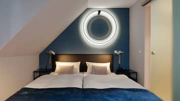 A modern bedroom with a large bed, a circular light fixture on the ceiling, and a dark blue accent wall.