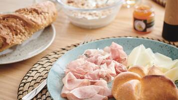 A breakfast setting with a plate of ham, cheese, and bread, a bowl of cereal, a glass of orange juice, and a jar of jam on a wooden table.