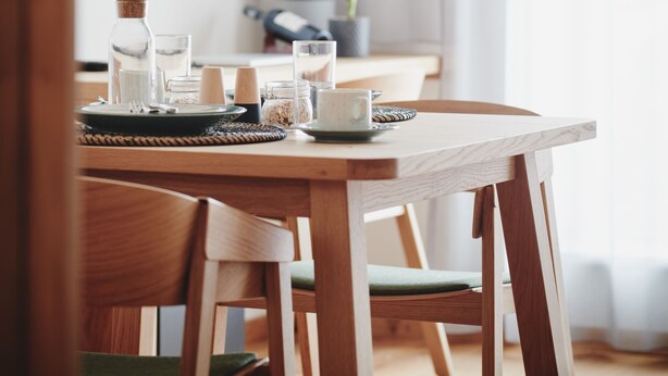 Uma sala de jantar com uma mesa de madeira, cadeiras, uma vela e um vaso com planta.