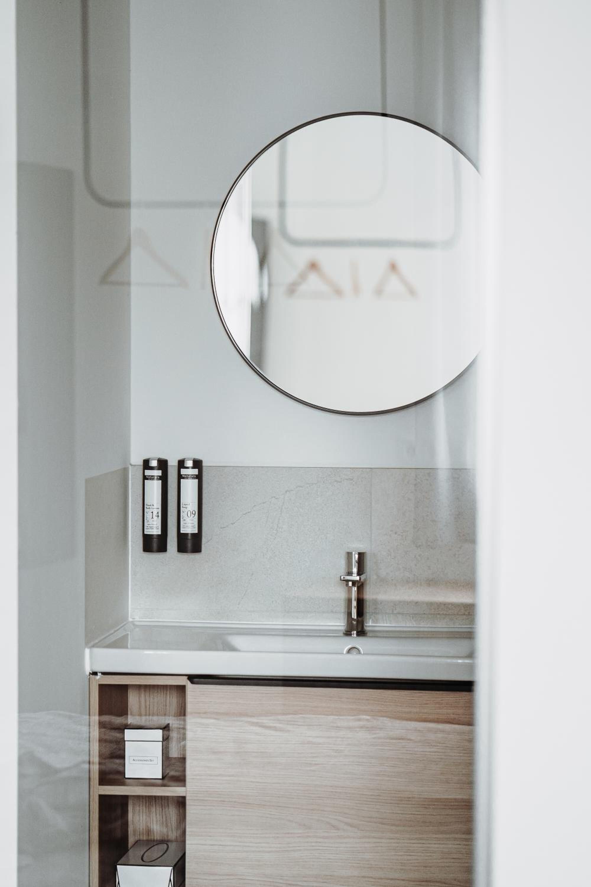 A bathroom with a round mirror, a sink, and two toiletry bottles.