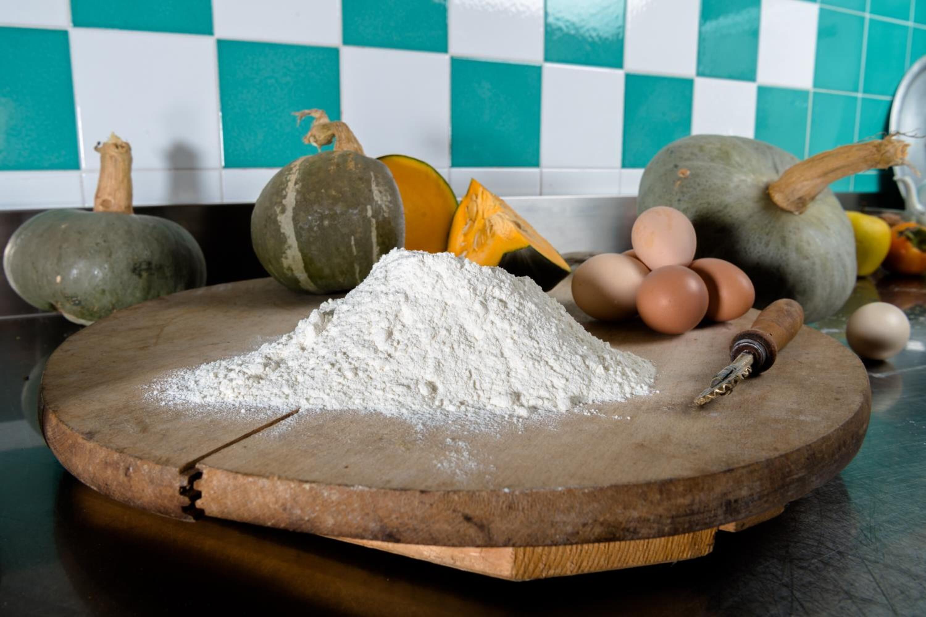 Una tabla de madera con harina, huevos y calabazas sobre una encimera de cocina.