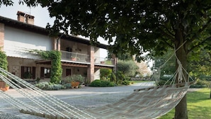 A hammock tied to a tree in a garden area with a building in the background. - Le Rondini (Bagnolo Mella)