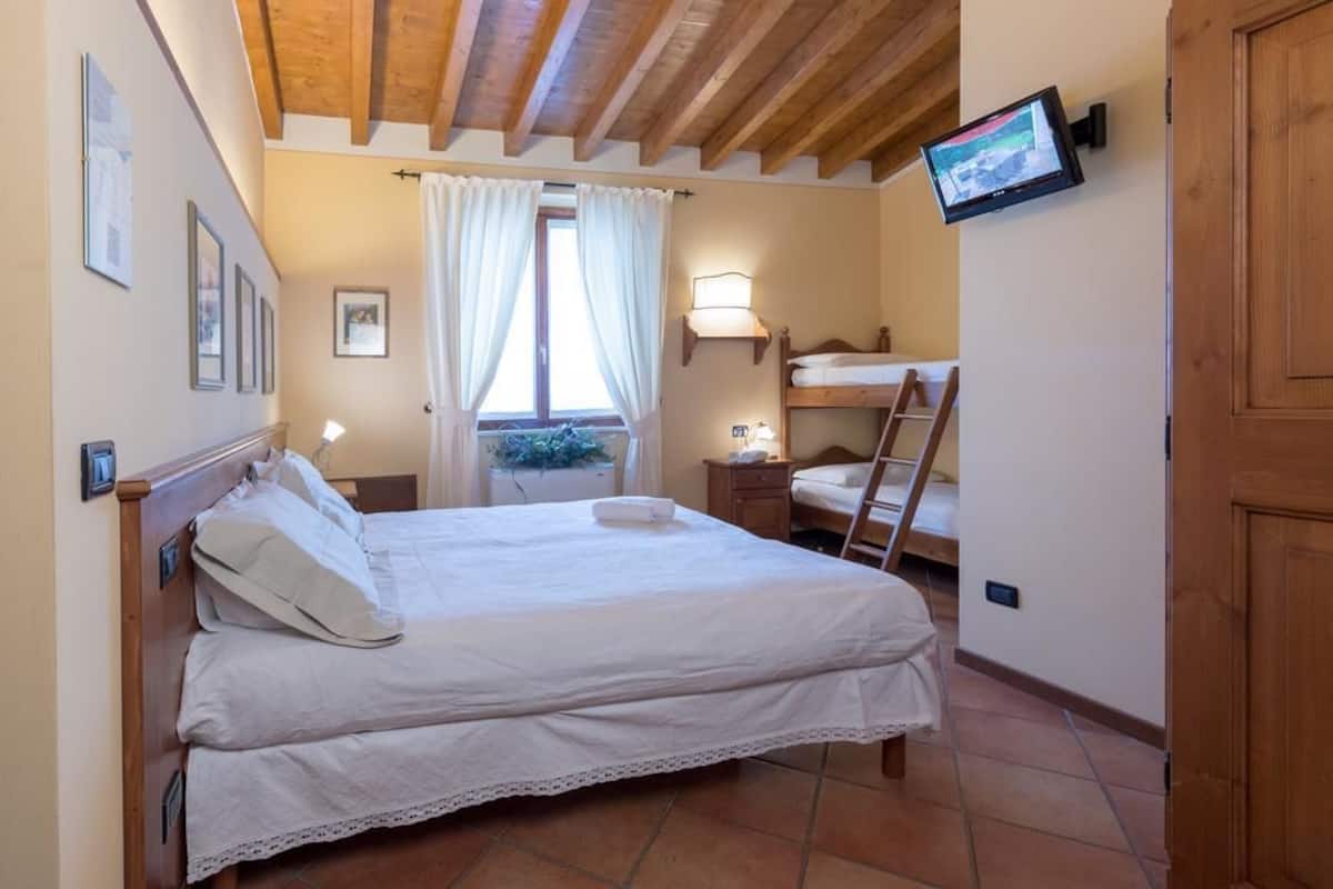 A bedroom with a double bed, a bunk bed, a TV mounted on the wall, and a window with curtains.