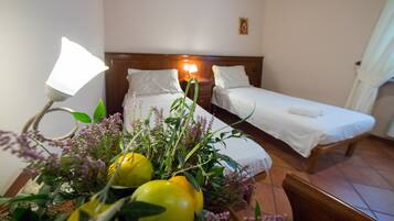 Camera d'albergo con due letti singoli, un comodino con una lampada e un bouquet di fiori sul tavolo.