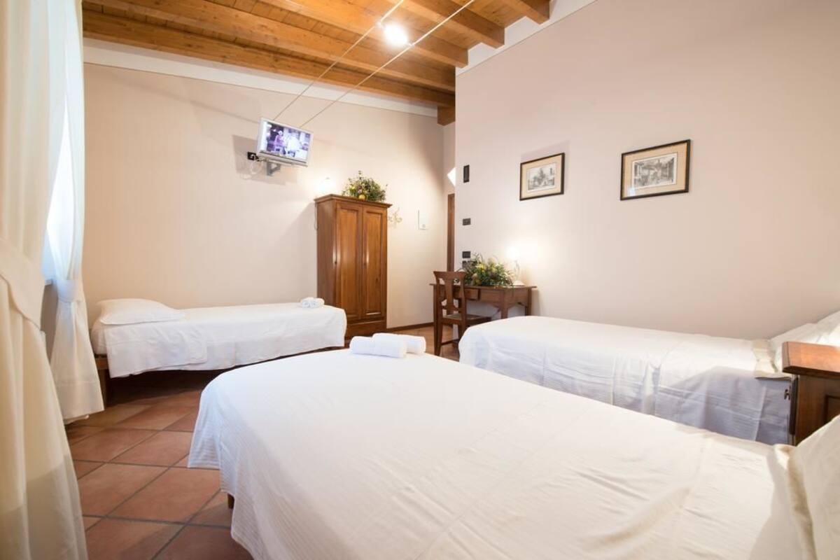 A hotel room with two single beds, a wooden cabinet, a television mounted on the wall, and two framed pictures on the wall.