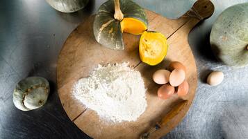 Una tabla de madera con harina, huevos y una calabaza sobre una superficie metálica.