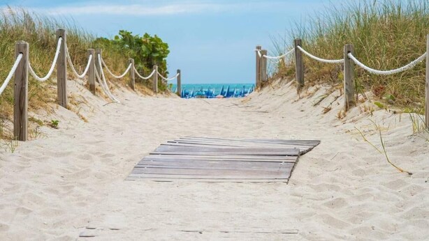 A wooden pathway leading to a beach with a rope barrier.