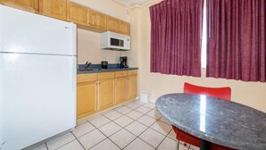 A compact kitchen with wooden cabinets, a white refrigerator, a microwave, and a small dining table with red chairs.
