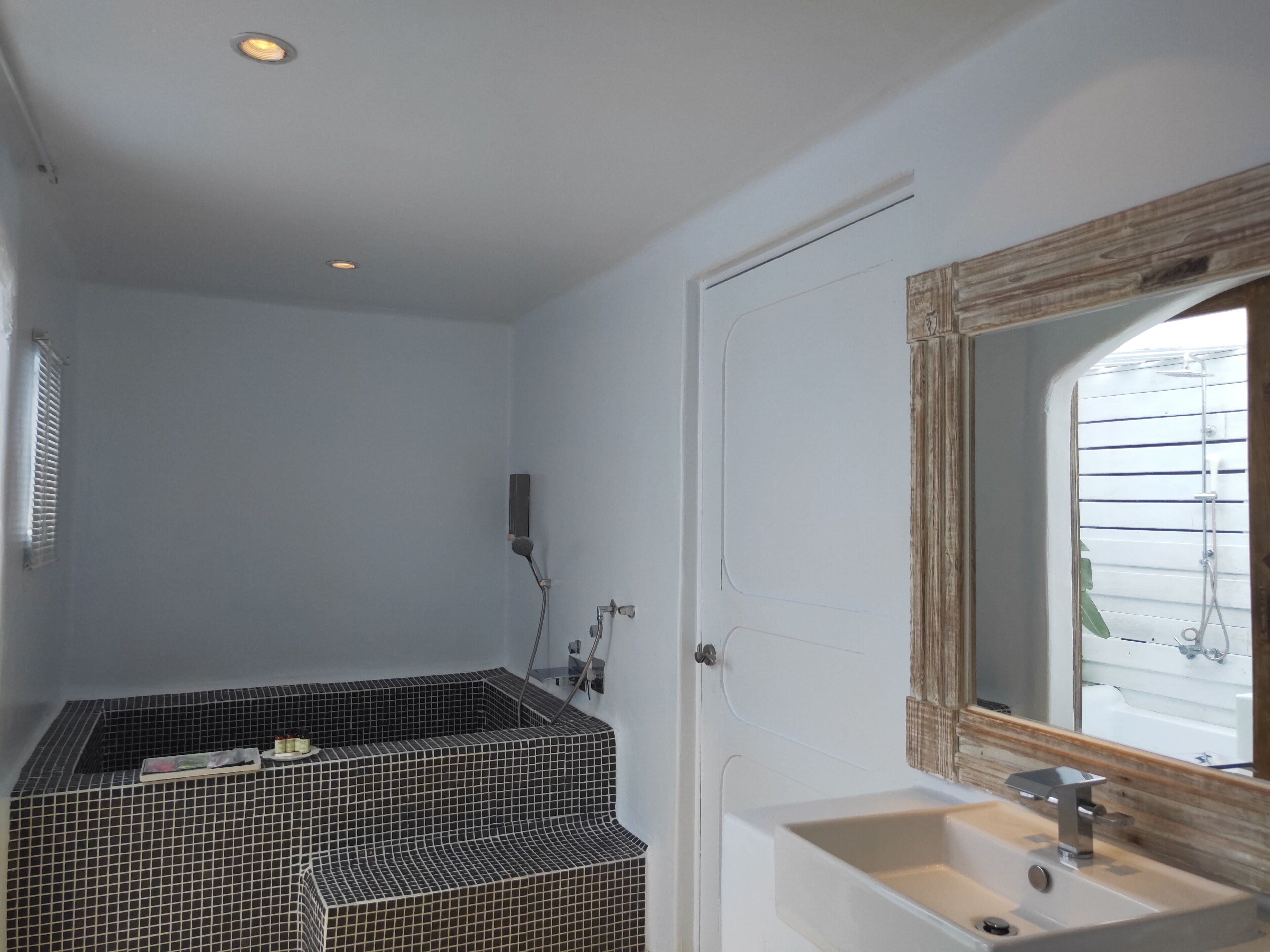 A bathroom with a tiled shower area, a sink with a mirror, and a window with blinds.