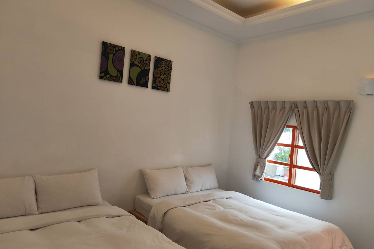 Habitació amb dos llits, una finestra amb cortines i tres quadres penjats a la pared.