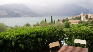 A view of a lake with mountains in the background, a town with buildings, and a chair in the foreground. - Apartment Enchanting Lake View, convenient to the Center and the Beaches (Malcesine)