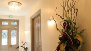 Un pasillo con una araña, una consola de madera con un arreglo floral y una puerta con paneles de vidrio esmerilado.