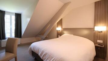 Una habitación de hotel con una cama grande, una silla, un escritorio y dos lámparas fijadas a la pared.