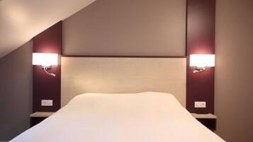 Habitación de hotel con una cama grande, dos mesitas de noche fijadas a la pared y un cabecero moderno.