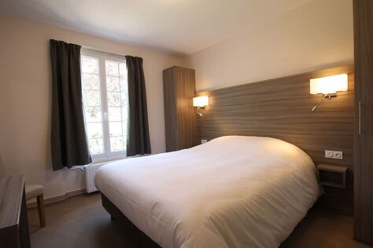 Une chambre d’hôtel avec un grand lit, une fenêtre avec des rideaux, une table de chevet et des lampes fixées au mur.