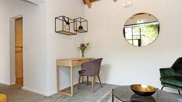 A modern room with a wooden desk, a green chair, a round mirror, and a glass coffee table with a bowl.