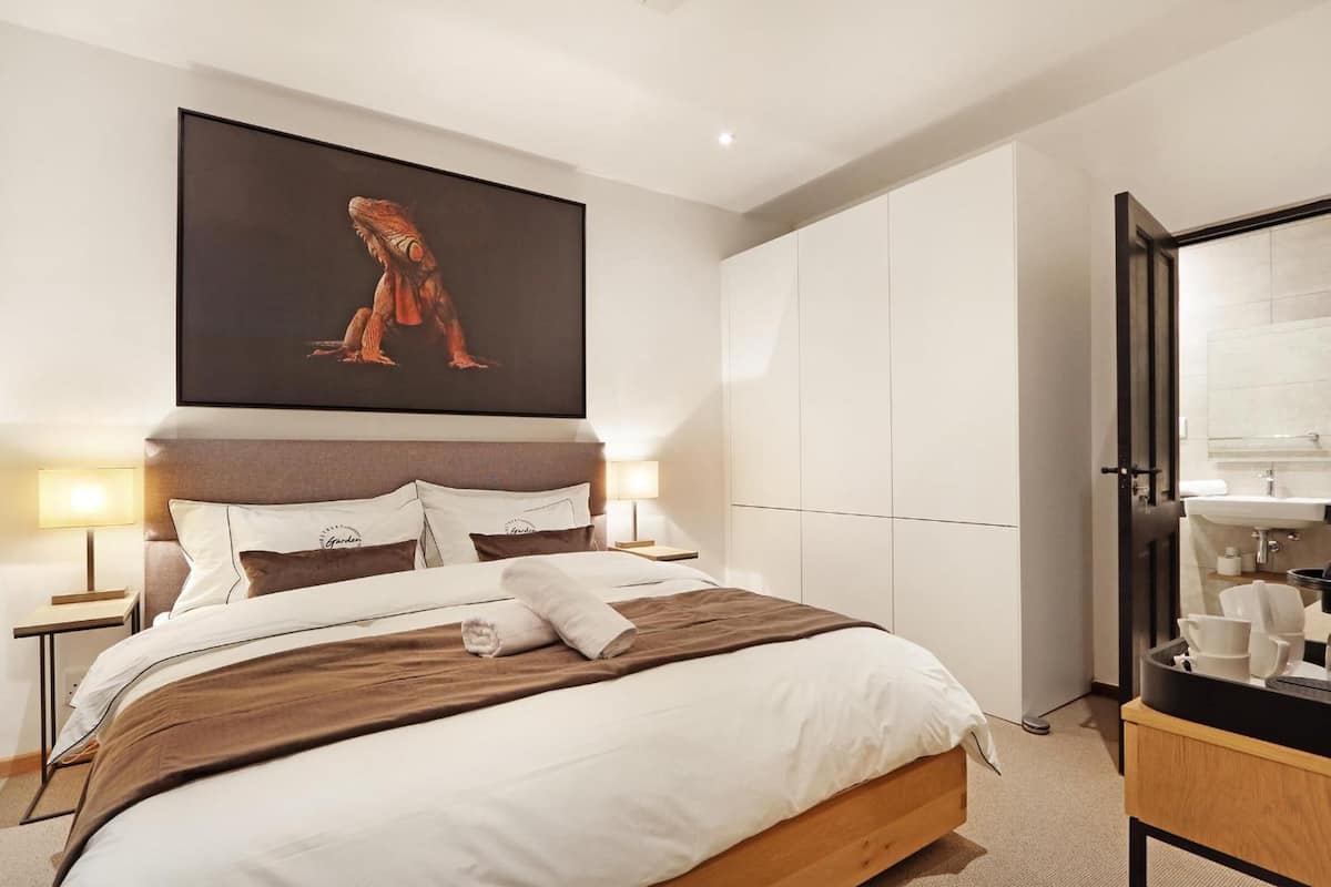 Een moderne hotelkamer met een groot bed, een nachtkastje met lamp, een kledingkast en een badkamer met wastafel en spiegel.