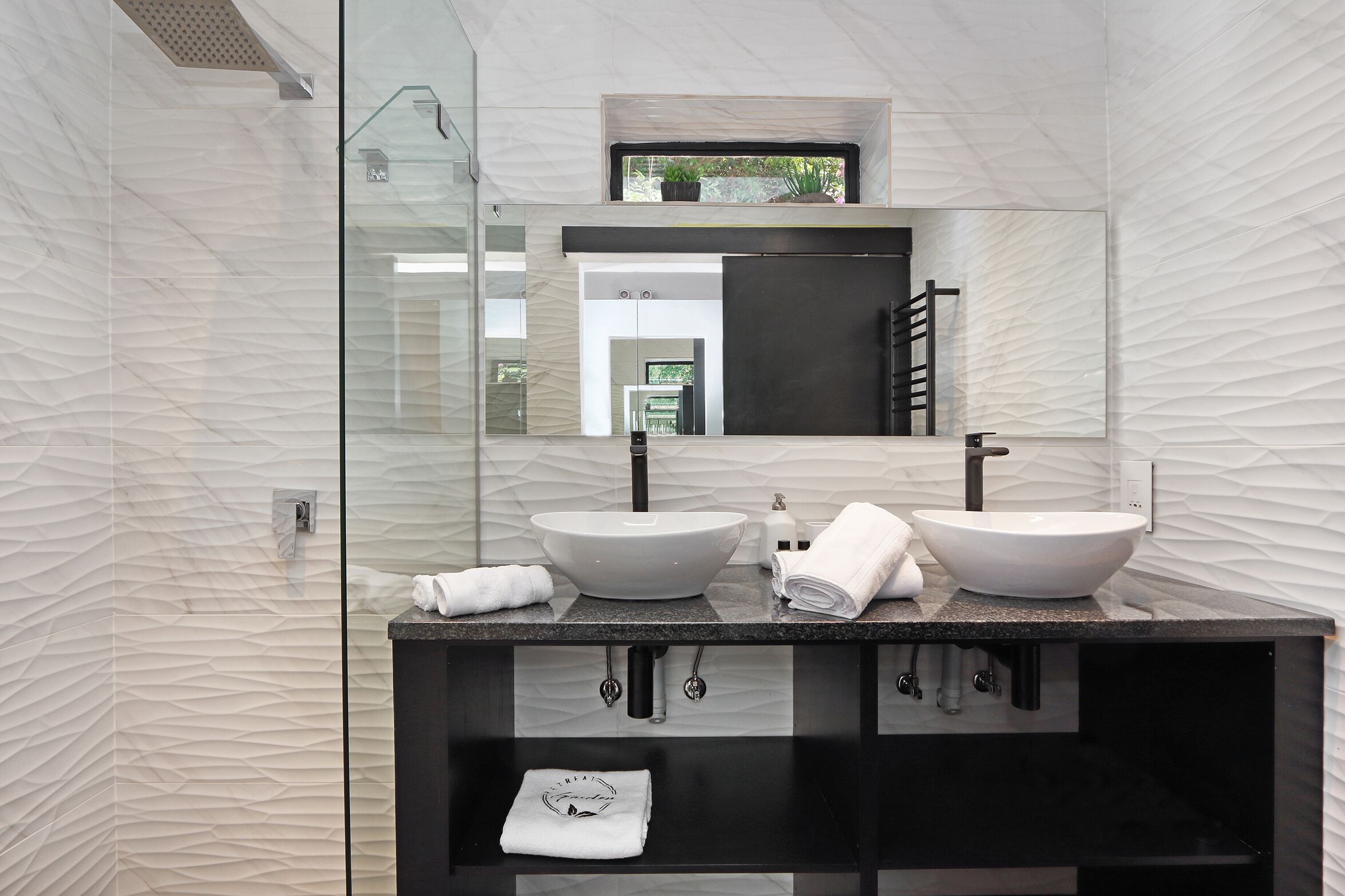 A modern bathroom with two vessel sinks, a large mirror, and a glass shower enclosure.