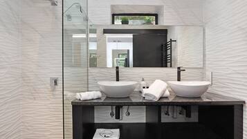 A modern bathroom with two vessel sinks, a large mirror, and a glass shower enclosure.