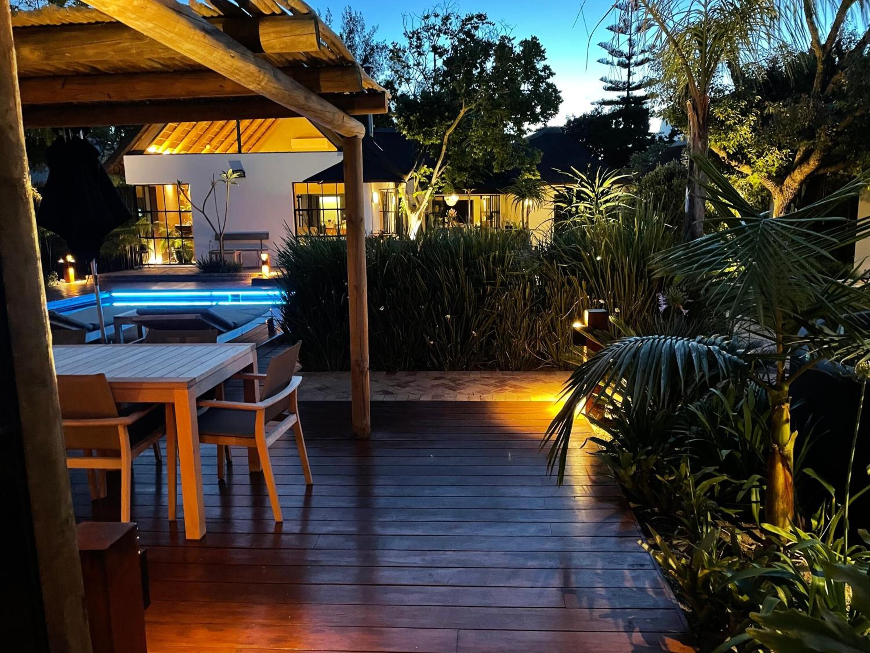 A wooden deck with a pool, outdoor seating, and lush greenery.