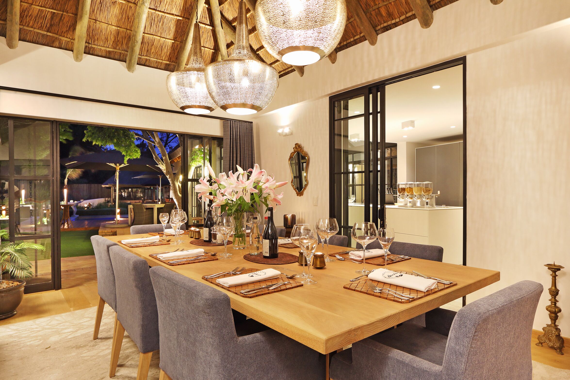 A dining area with a long wooden table set for a meal, surrounded by grey upholstered chairs.