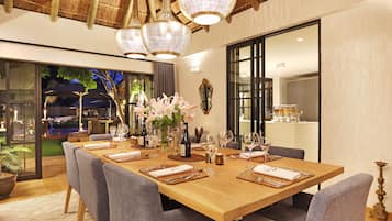 A dining area with a long wooden table set for a meal, surrounded by grey upholstered chairs.