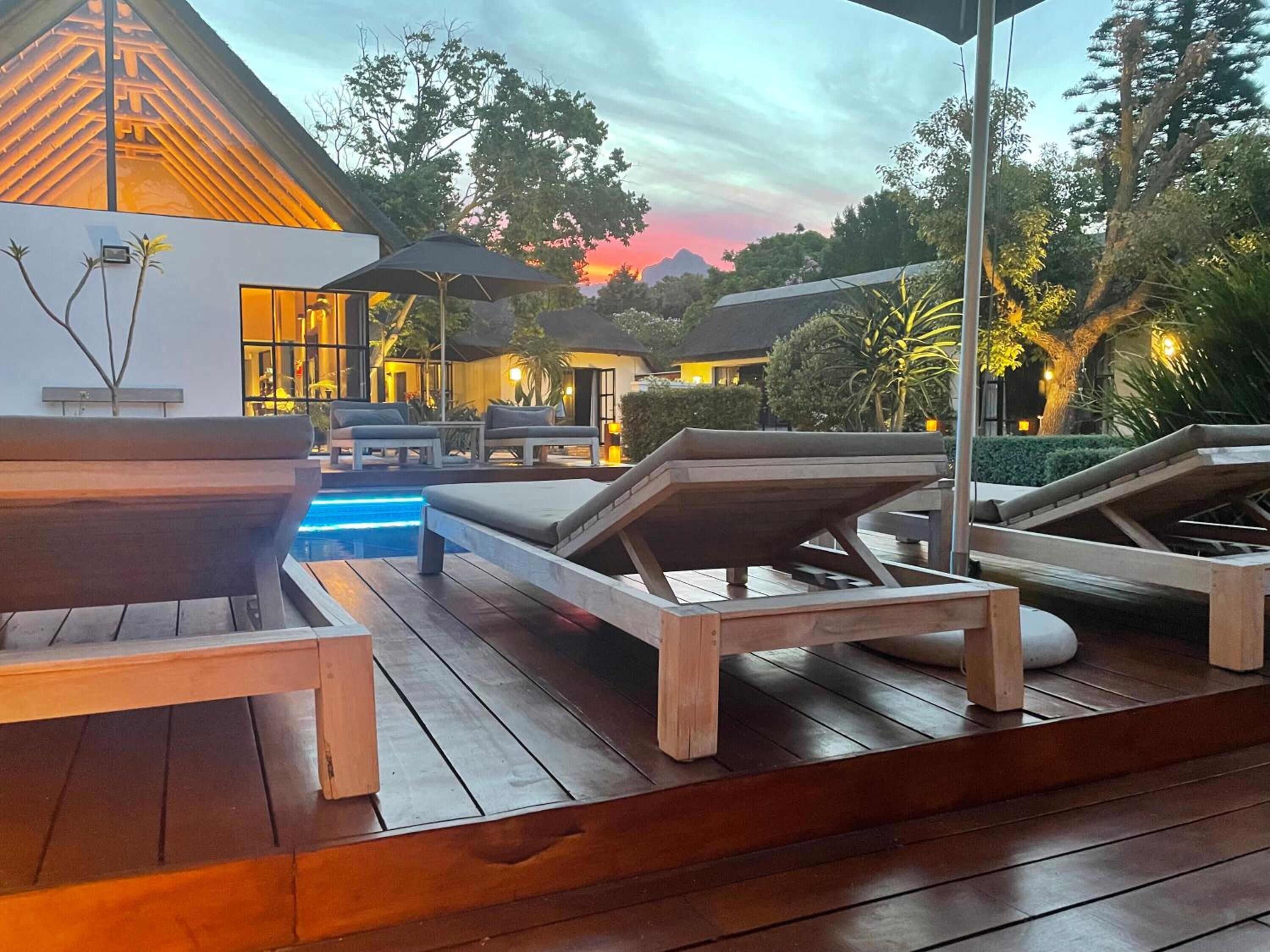 Un espace aménagé au bord de la piscine, avec des chaises longues en bois, une petite piscine et un bâtiment doté d’un toit en pente.