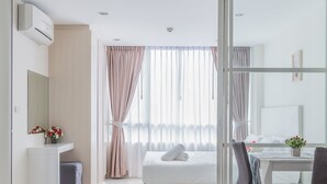 Una habitación de hotel moderna con cama, escritorio y silla. Hay una ventana con cortinas, un espejo y una pequeña planta en el escritorio.