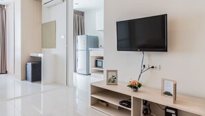 Ein modernes Hotelzimmer mit einem an der Wand befestigten Flachbildfernseher, einer kleinen Holztruhe mit Dekorationen, einem kompakten Kühlschrank und einer Mikrowelle.