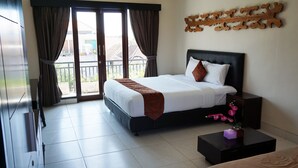 A hotel room with a bed, a nightstand, a small table with a vase, and a view of the outside through a sliding door.