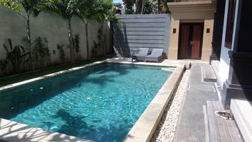 A rectangular swimming pool with clear water, surrounded by a low stone border.