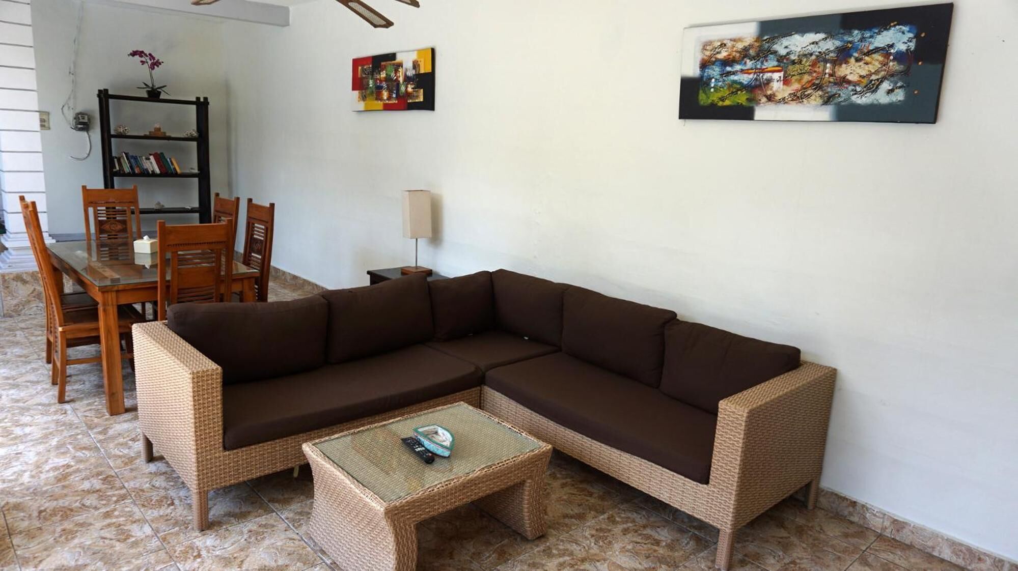A living room with a brown sectional sofa, a small wicker table, and a dining area with wooden chairs and a glass table.
