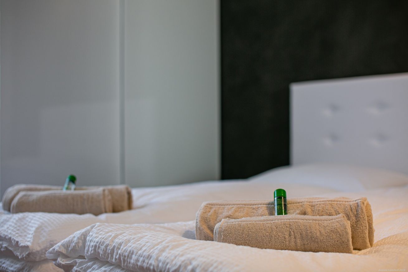 Een hotelkamer met keurig opgemaakte bedden, elk met een opgerolde handdoek en een groene fles.