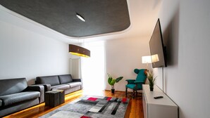 Un salon moderne avec un canapé gris, un fauteuil turquoise, une table basse, un téléviseur fixé au mur et un tapis à motifs.