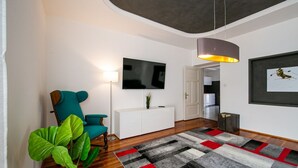 Un salon moderne avec un fauteuil turquoise, une console blanche, un grand téléviseur à écran plat, un tapis à motifs et une suspension.