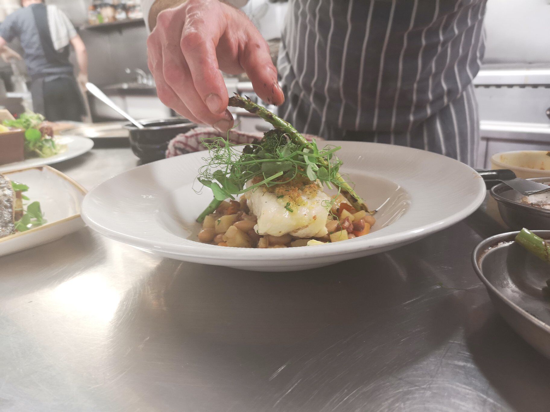 A chef preparing a dish with a white plate, a spoon, and a kitchen counter.
