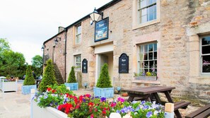 A stone building with multiple windows and a welcoming entrance. There are flower beds with colorful flowers in front of the building. - The Fleece Inn (Lancaster)