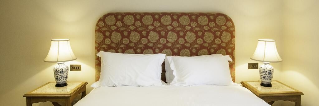 A neatly made bed with white linens and two bedside lamps with floral patterns.