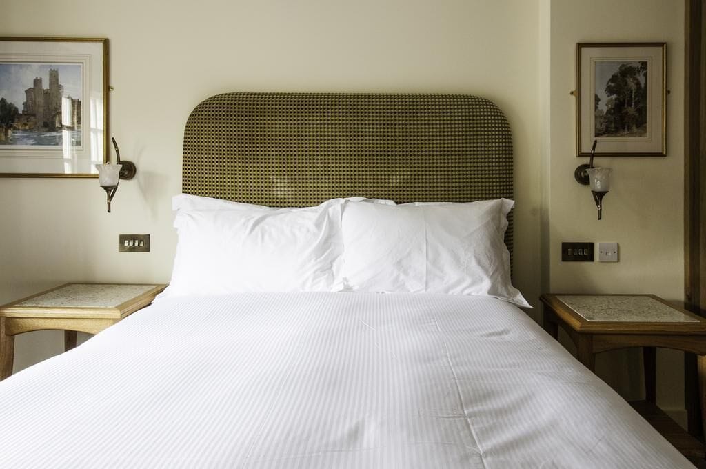 A neatly made bed with white linens, a woven headboard, and two bedside tables with lamps.