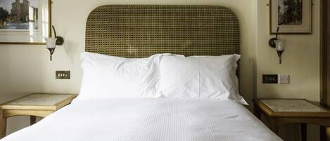 A neatly made bed with white linens, a woven headboard, and two bedside tables with lamps.