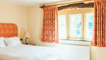 A hotel room with a bed, a nightstand, a lamp, a window with curtains, and a painting on the wall.