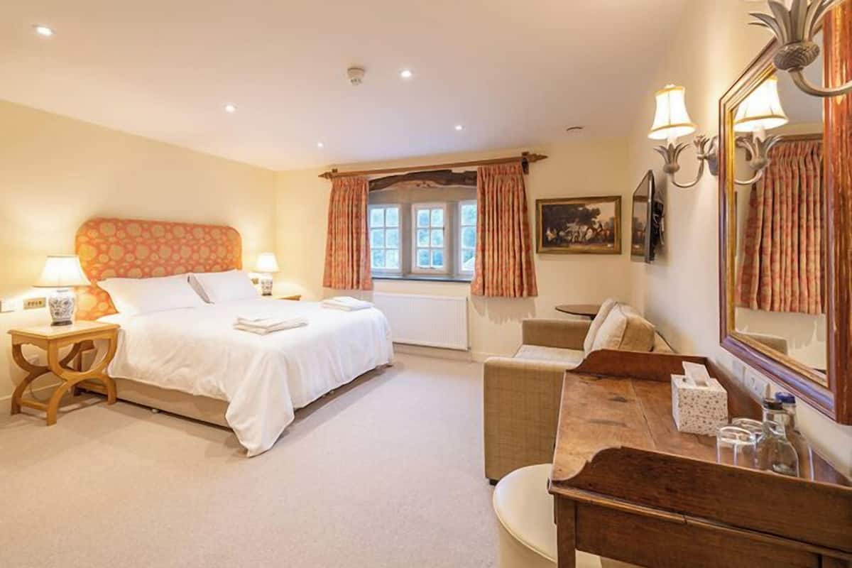 A bedroom with a bed, bedside tables, a desk, a chair, a window with curtains, and a mirror.