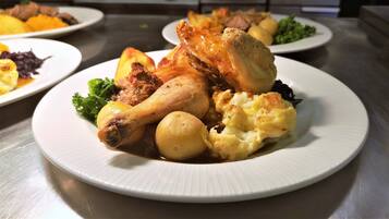 Un plato con pollo asado, papas y una guarnición de verduras.