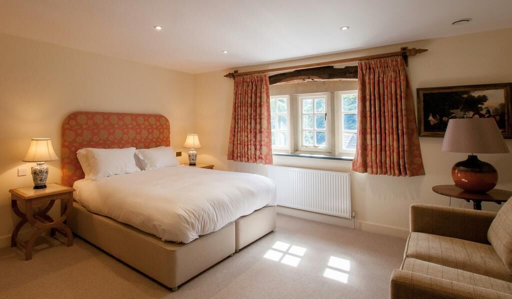 A bedroom with a bed, two bedside tables with lamps, a window with curtains, a radiator, and a chair.