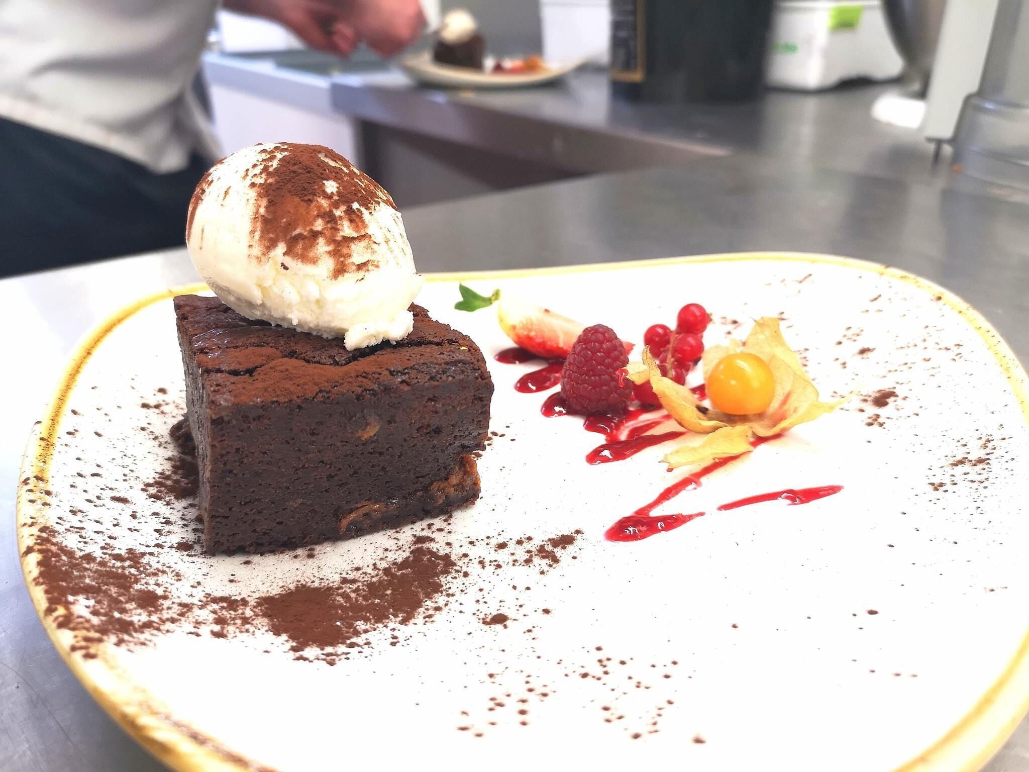 A dessert plate with a brownie, ice cream, raspberries, and a cherry.