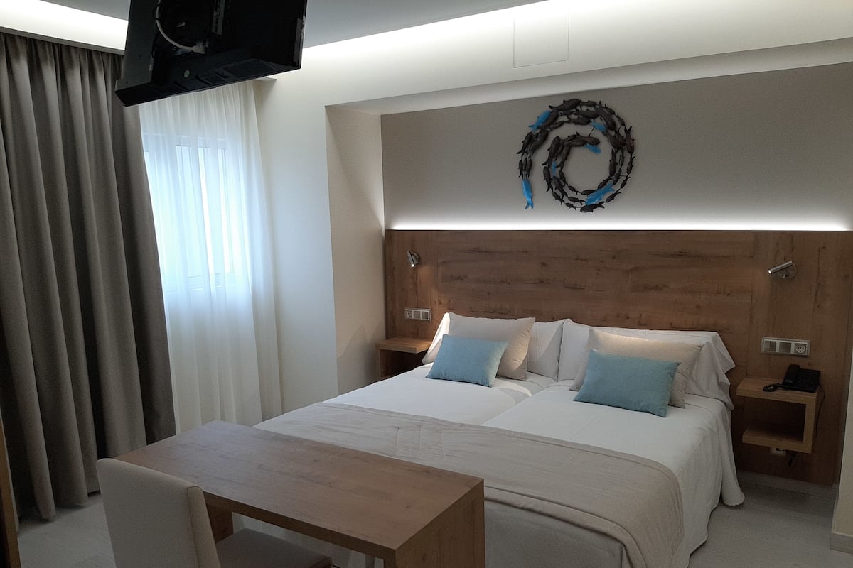 A modern hotel room with a large bed, a wooden nightstand, a desk, and a chair.