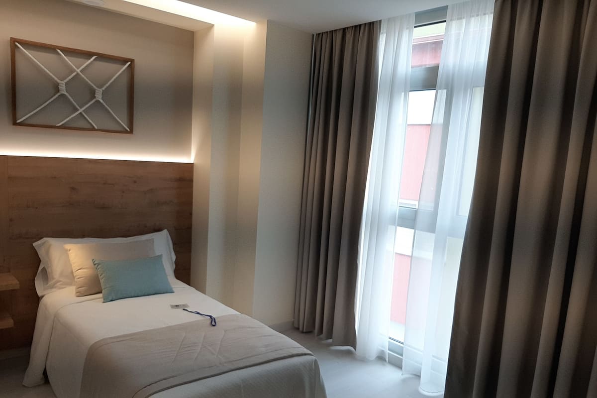 A hotel room with a bed, a headboard, a wall-mounted artwork, and a window with curtains.